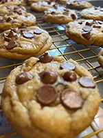 imagery of chocolate chip cookies cooling on a gold cooling rack